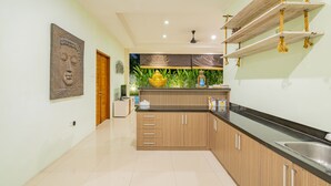 Una cocina moderna con armarios de madera, una encimera negra y un lavamanos. Se observa una estatua de Buda y un tapiz decorativo.