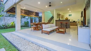 Un moderno espacio de sala con sofá, una mesa de comedor y sillas, una cocina con taburetes de bar y una escalera que sube a un nivel superior.