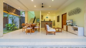 Amplia sala de estar con una mesa de comedor, sillas, un sofá, un televisor y una escalera que lleva a un nivel superior.