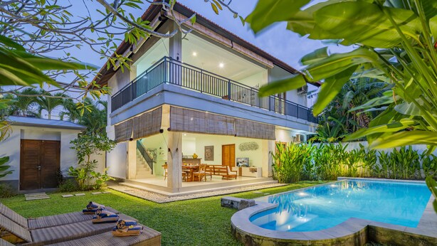 Una casa de dos plantas con un balcón, piscina y jardín bien cuidado.