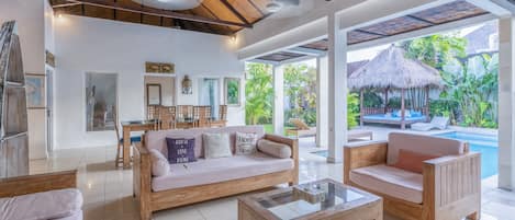 A spacious living area with a large sofa, wooden coffee table, and a view of a pool and outdoor seating area.