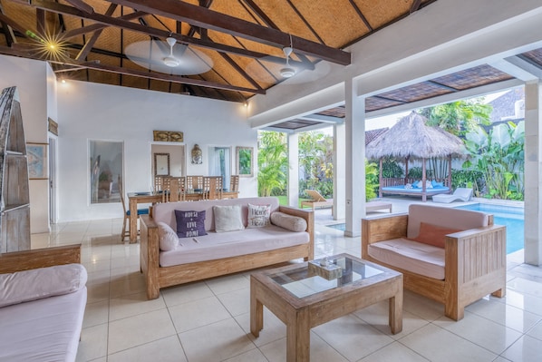 A spacious living area with a large sofa, wooden coffee table, and a view of a pool and outdoor seating area.
