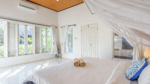 Un dormitorio amplio con una cama grande, cortinas blancas y vistas a la vegetación.