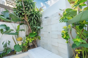 A small, enclosed shower area with tiled walls and a step leading into it, surrounded by lush green plants. - AV Villa Jasmin (Seminyak)