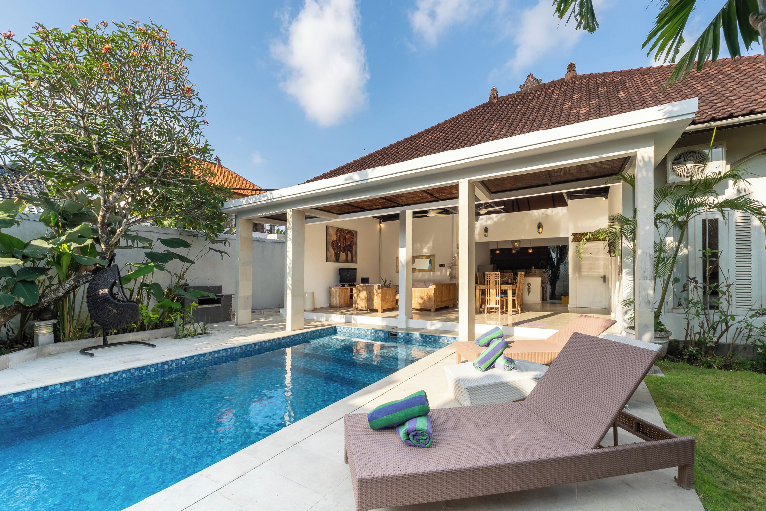 Un espace aménagé au bord de la piscine, avec des chaises longues, un patio couvert et une vue sur l’intérieur.