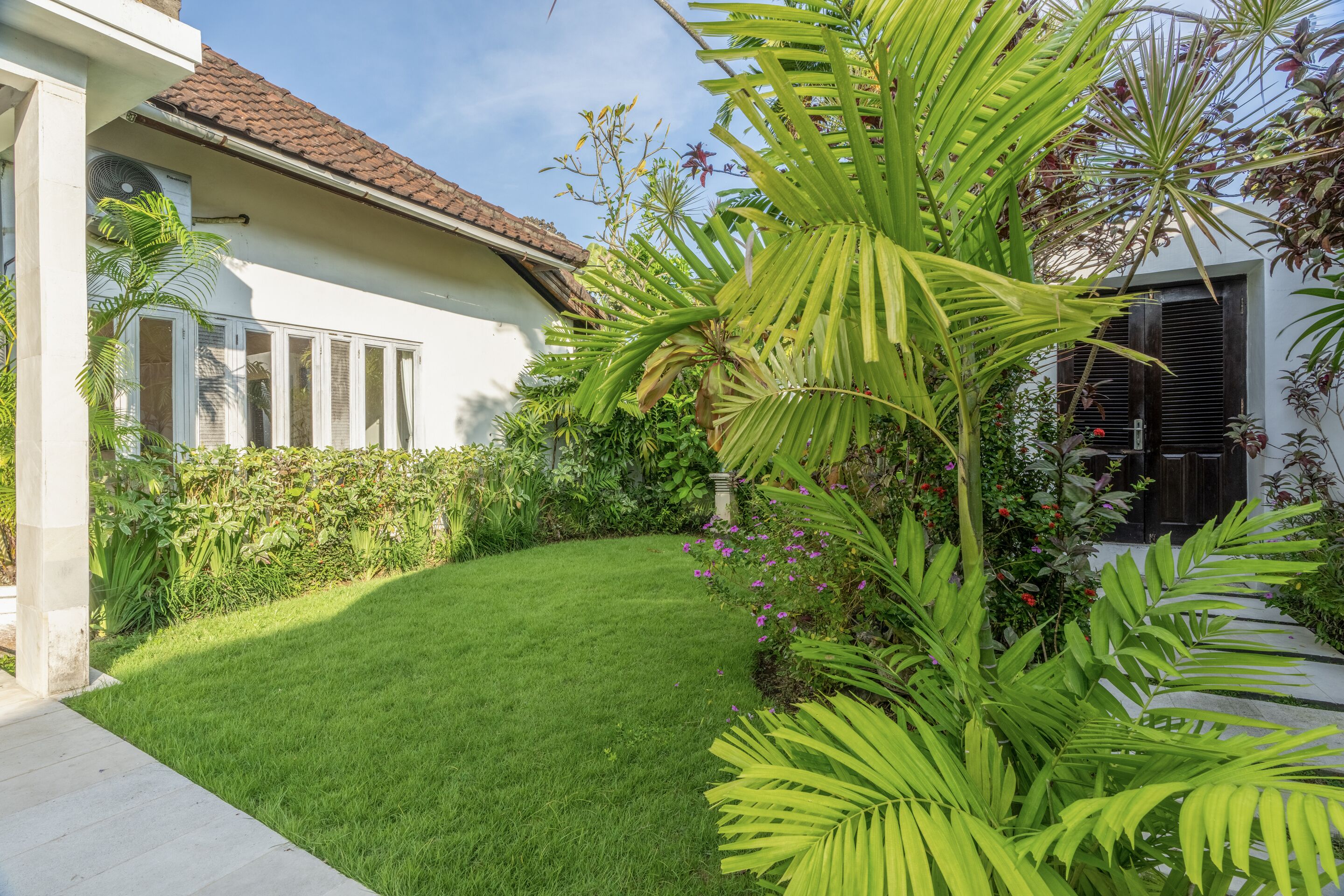 En velholdt have med græsplæne, forskellige planter og et hus med tegltag.