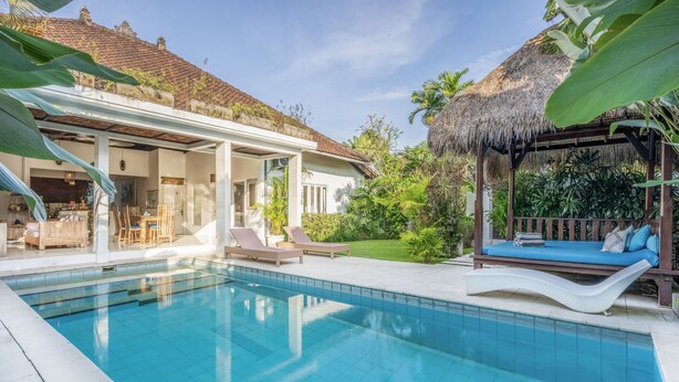 Una piscina con sillas de descanso, un patio cubierto y una estructura con techo de paja.