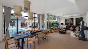Ein geräumiger Wohnbereich mit Esstisch für vier Personen, einem großen Fenster mit Blick auf einen Pool und einer Statue in der Ecke.