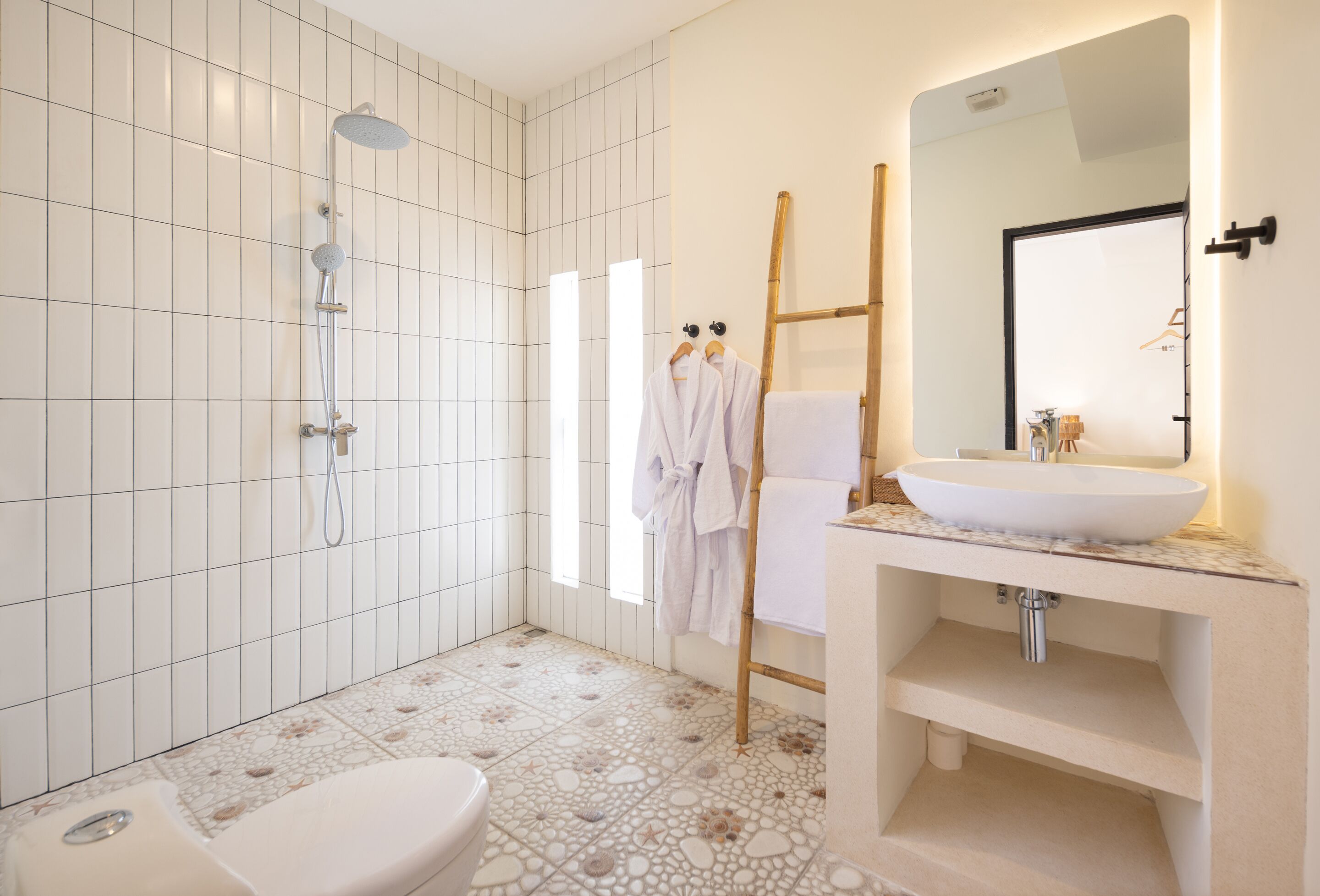 Un bagno moderno con doccia in piastrelle bianche, vaso sospeso e un mobile lavabo con un grande specchio.