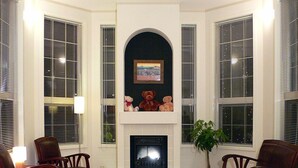 Uma sala de estar com lareira, duas poltronas, uma mesa e um vaso de planta.