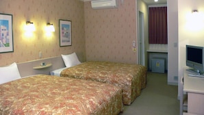Habitación de hotel con dos camas, un escritorio pequeño con lámpara, un televisor y un equipo de aire acondicionado.