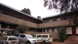 Un edificio con fachada de ladrillo, múltiples ventanales y un estacionamiento techado con tres vehículos.