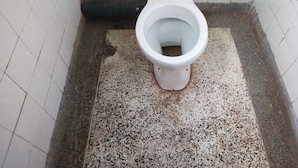 Un baño pequeño con azulejos, un inodoro blanco, un desagüe a la vista y una tubería verde en la pared.