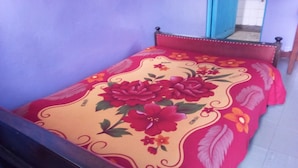 Una cama con colcha floral y cabecera de madera en una habitación con suelo de baldosas blancas.