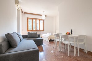 A modern room with a grey sofa, a bed, a dining table with chairs, and a window with wooden frames. - Novoli 4 Bedrooms by Mmega (Florence)