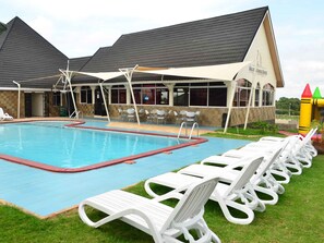 A swimming pool with lounge chairs and a covered area with tables and chairs. - Golden Gates Hotel (Mweiga)