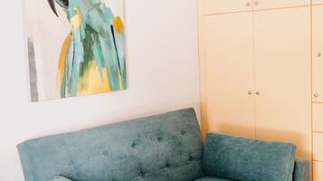 Un canapé de couleur turquoise, une armoire de couleur claire et un tableau représentant un perroquet accroché au mur.