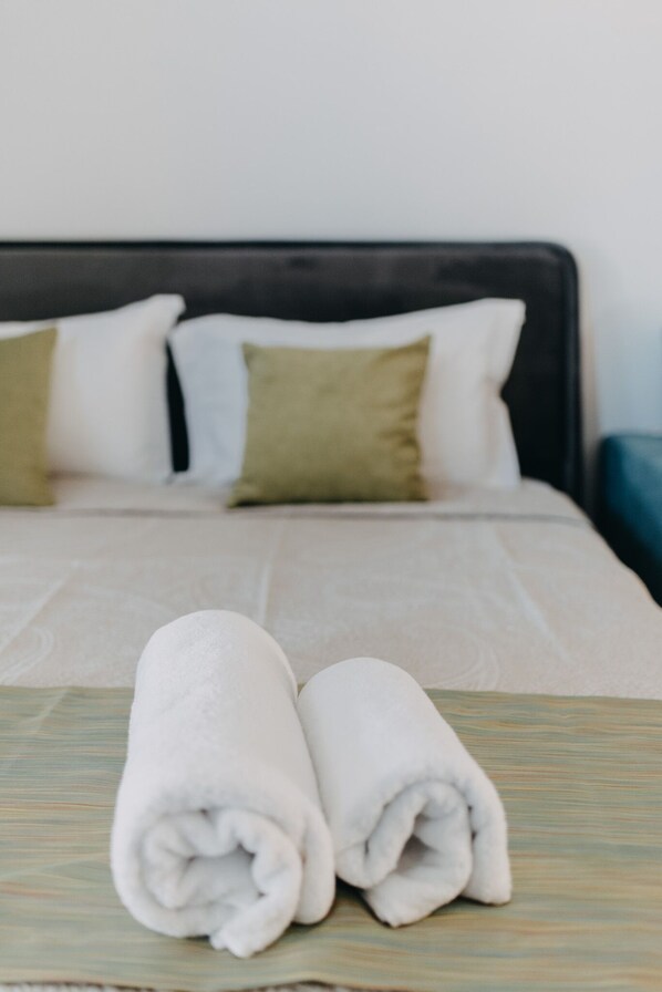 A neatly made bed with white and green pillows, and two rolled white towels on a patterned bedspread. - Best House- Nirvana II Patra (Patras)
