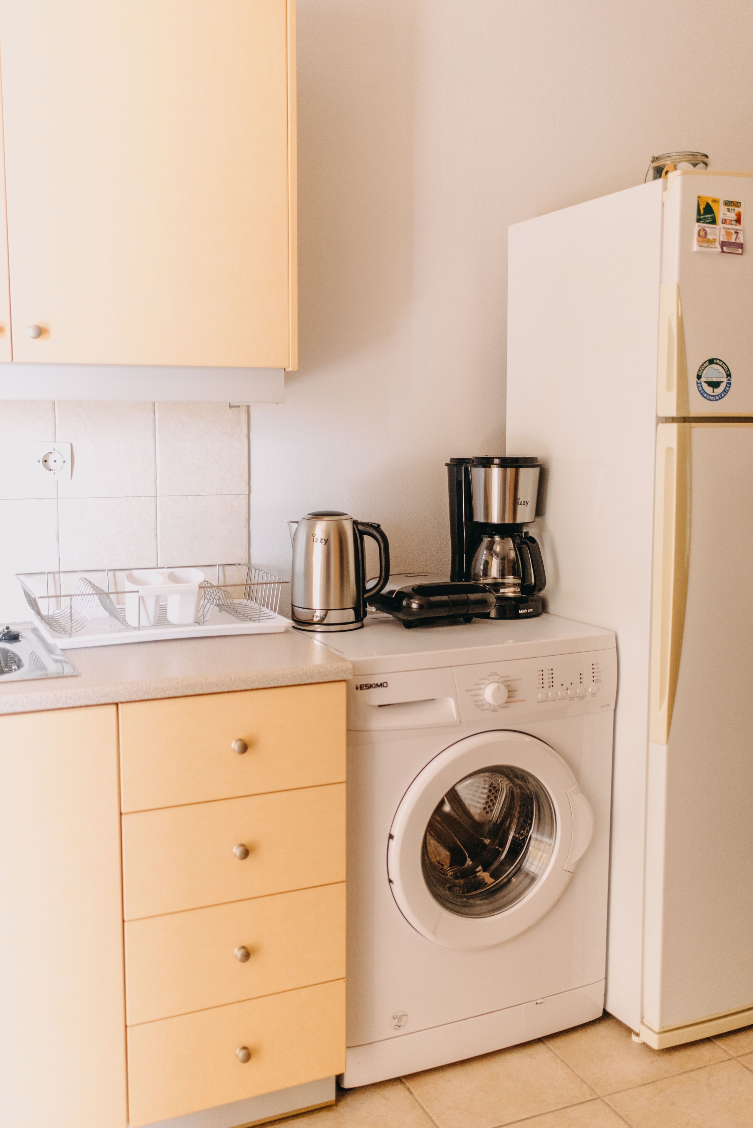 A compact kitchen with a washing machine, a coffee maker, and a refrigerator.
