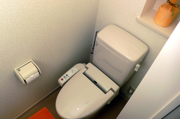 Un baño pequeño y moderno con inodoro, dispensador de toallas de papel y un estante con una vela.