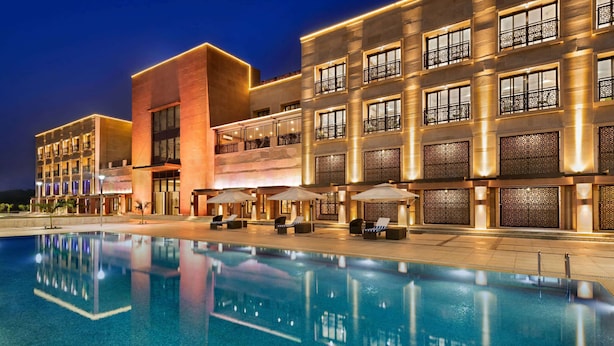 Een modern hotel met een zwembad, terras en een goed verlichte gevel.