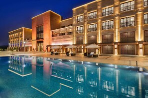 A modern hotel with a swimming pool, outdoor seating, and a well-lit facade. - Ramada Encore by Wyndham Statue of Unity (Garudeshwar)