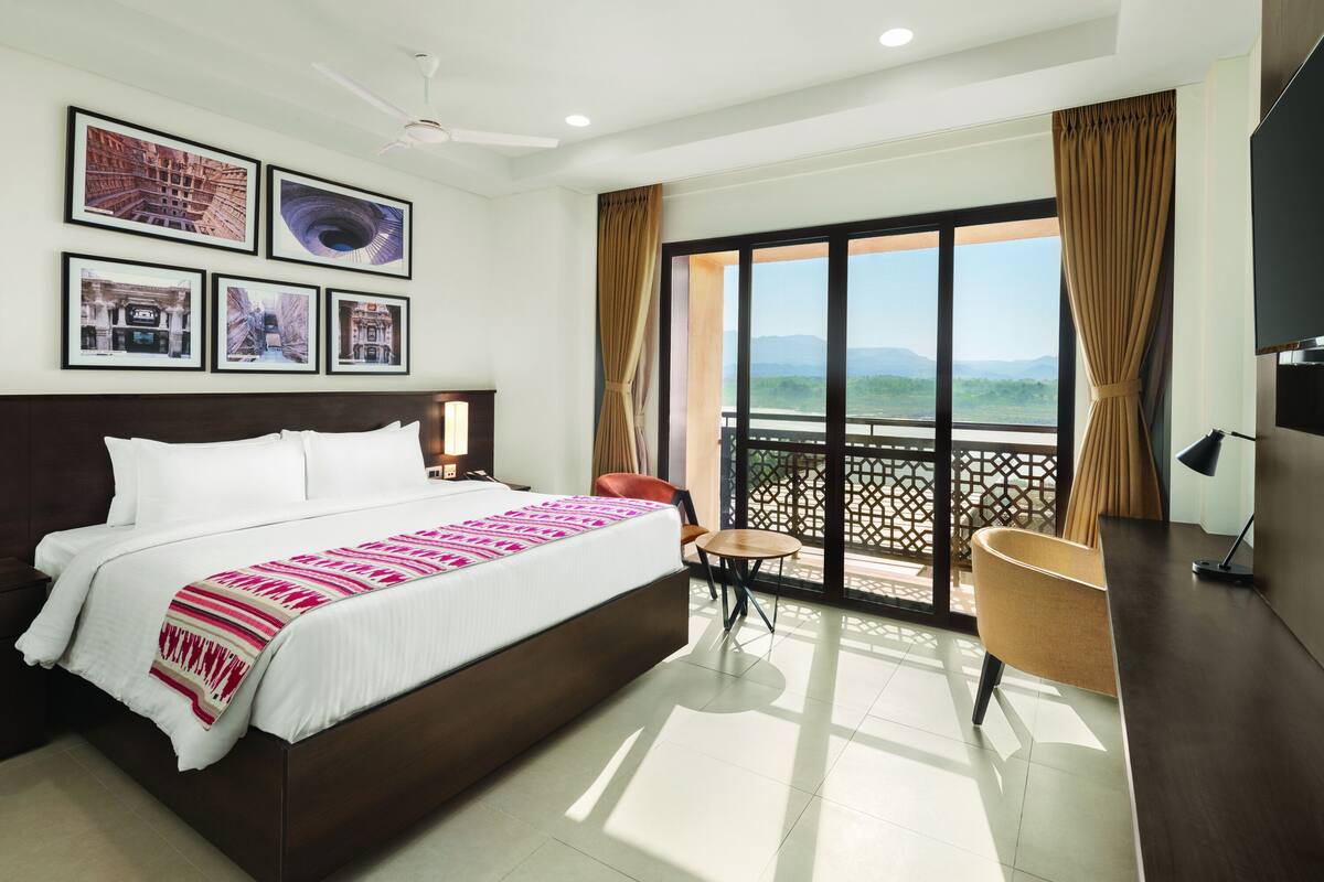 Habitación de hotel con una cama grande, un escritorio, una silla y un balcón con vistas.