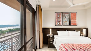 Een hotelkamer met een groot raam, een bed, een nachtkastje en een plafondventilator.