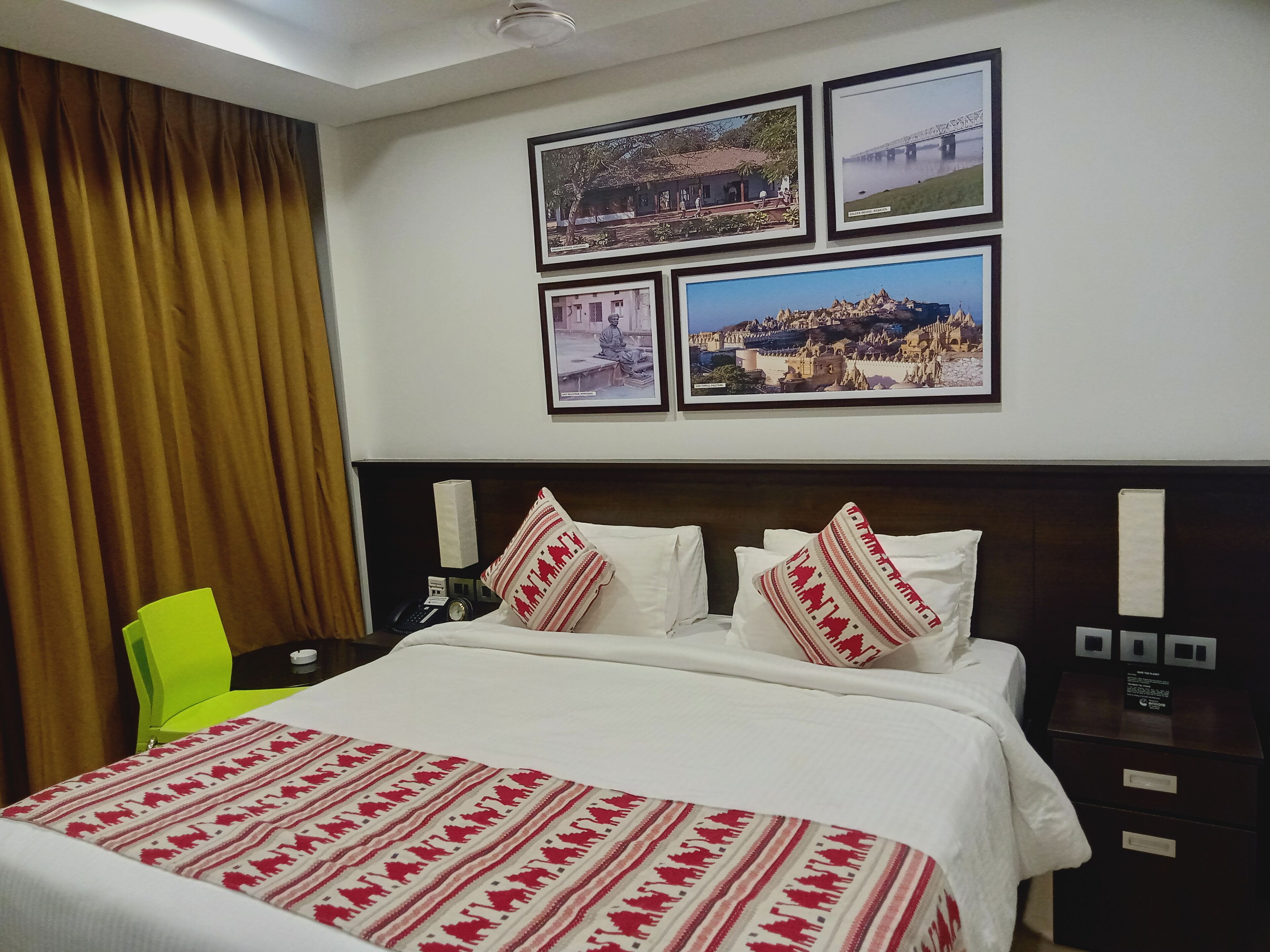 Une chambre d’hôtel avec un lit, une table de chevet, une chaise et un mur orné de tableaux.