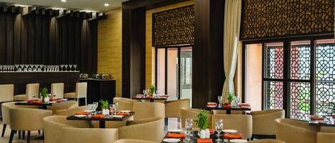A modern restaurant with multiple tables and chairs, a bar area, and decorative screens.