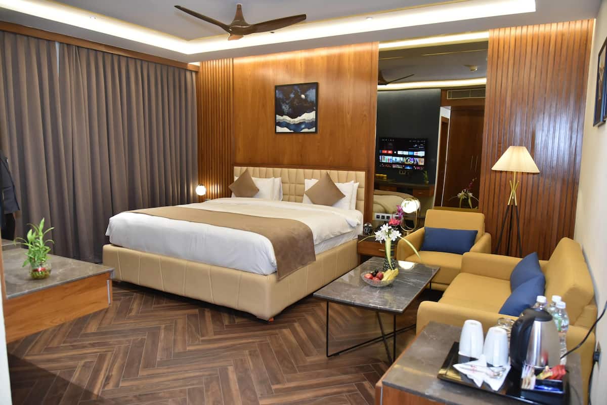 Una habitación de hotel con una cama grande, un sofá, una mesita con artículos de aseo y un televisor al fondo.