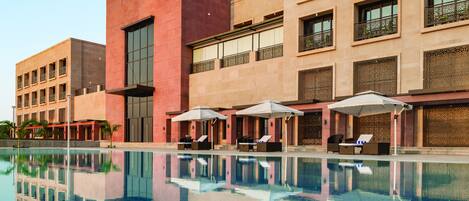 A modern hotel with a swimming pool, sun loungers, and a reflection of the building.
