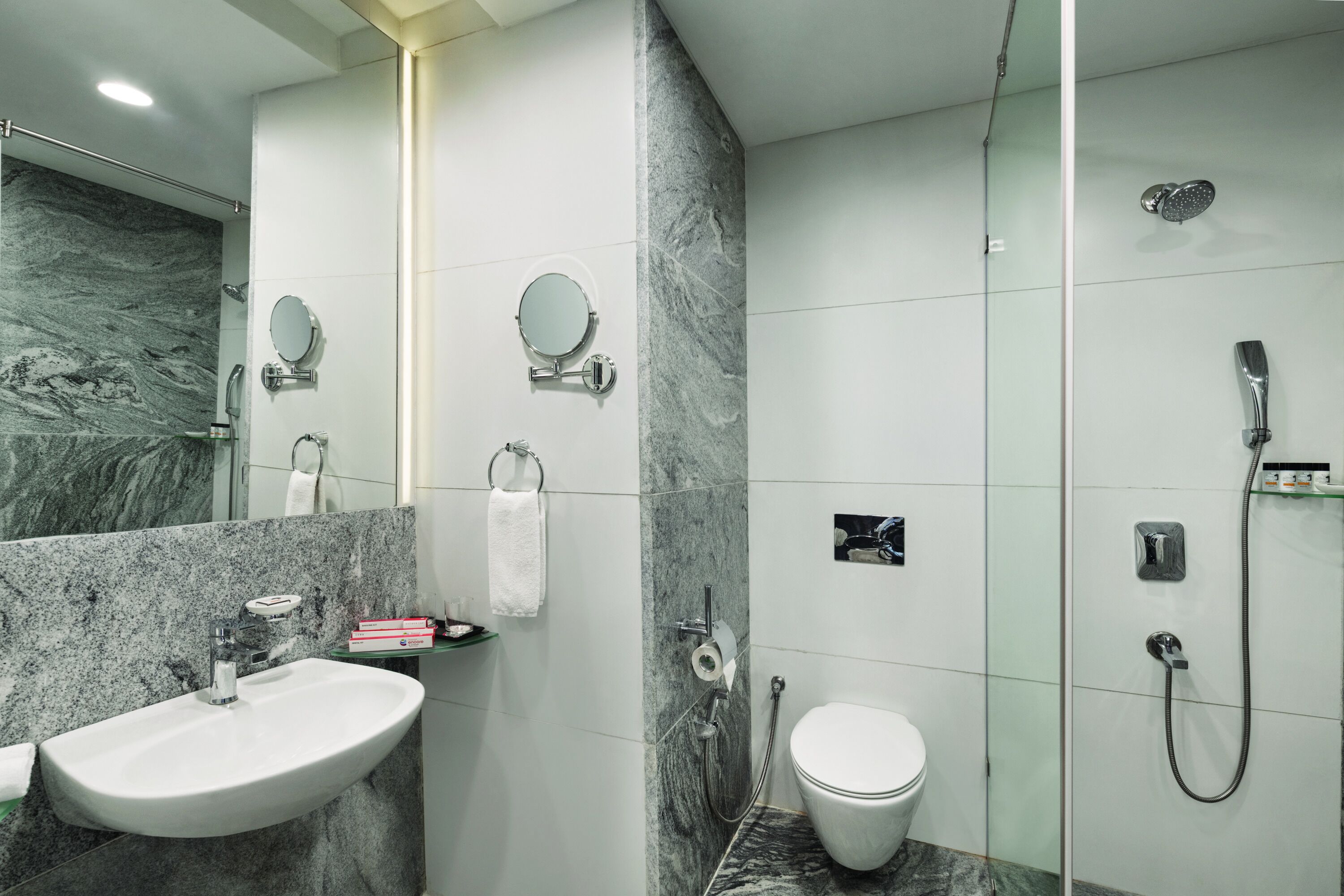 Un baño moderno con lavamanos de mármol, dos espejos fijos en la pared, inodoro y cabina de ducha con mampara de vidrio.