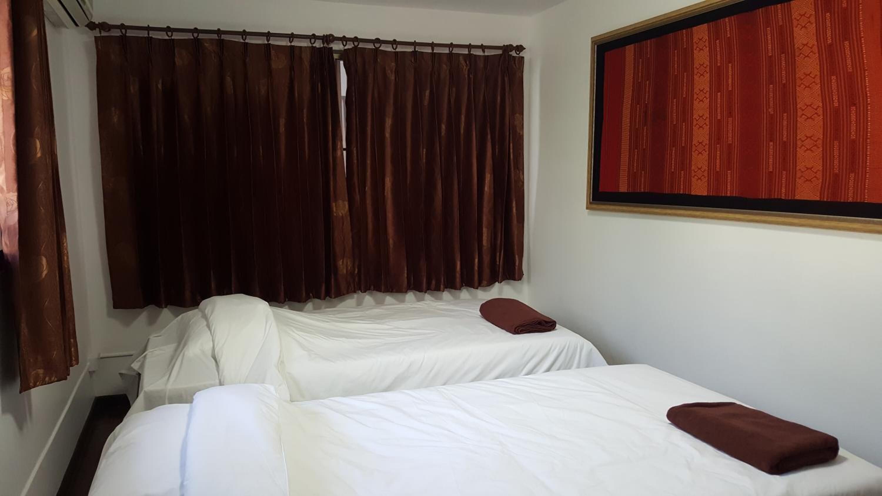 A room with two beds, a window with a red curtain, and a framed picture on the wall.
