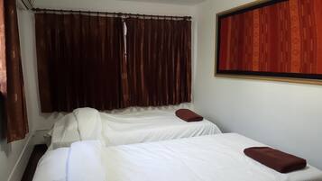 A room with two beds, a window with a red curtain, and a framed picture on the wall.