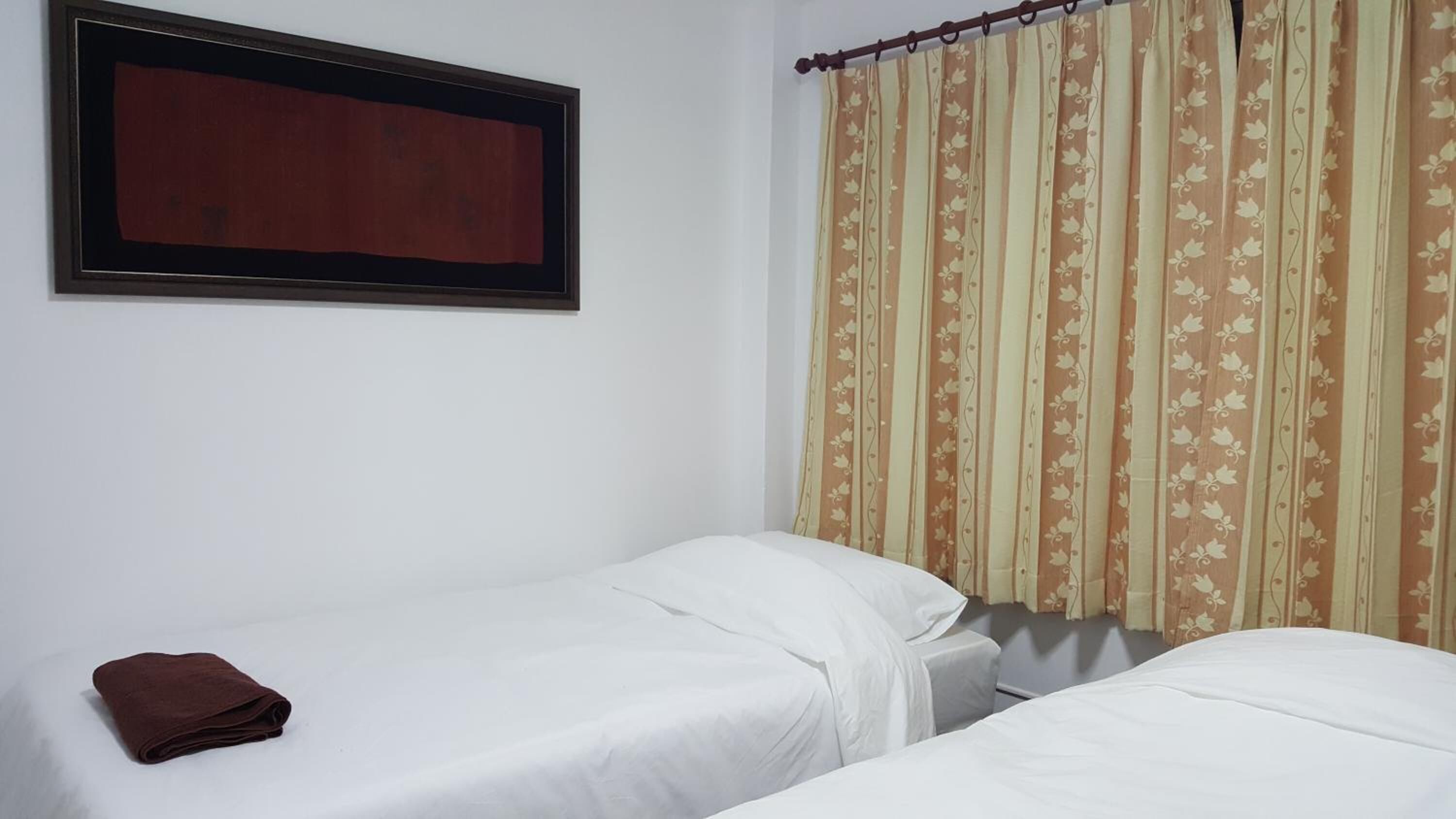 A simple room with two beds, a framed picture on the wall, and a curtain with a floral pattern.