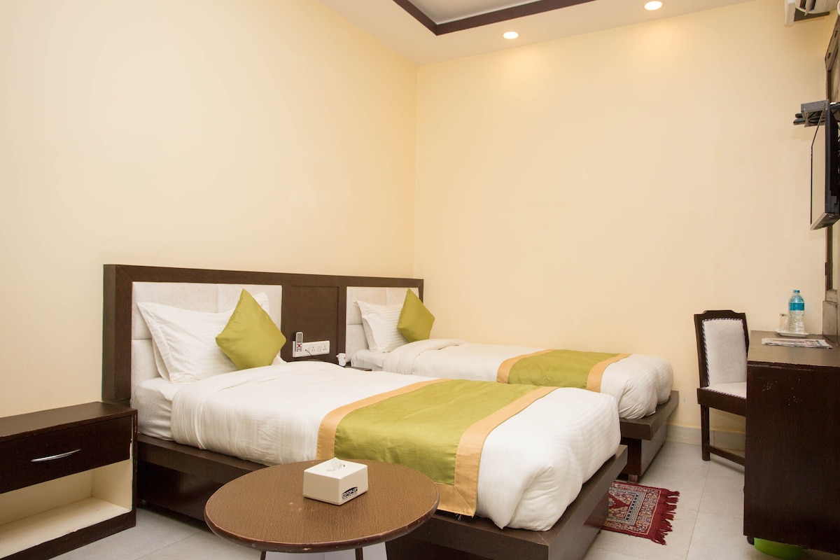 A hotel room with two beds, a small table, a desk, and a chair.