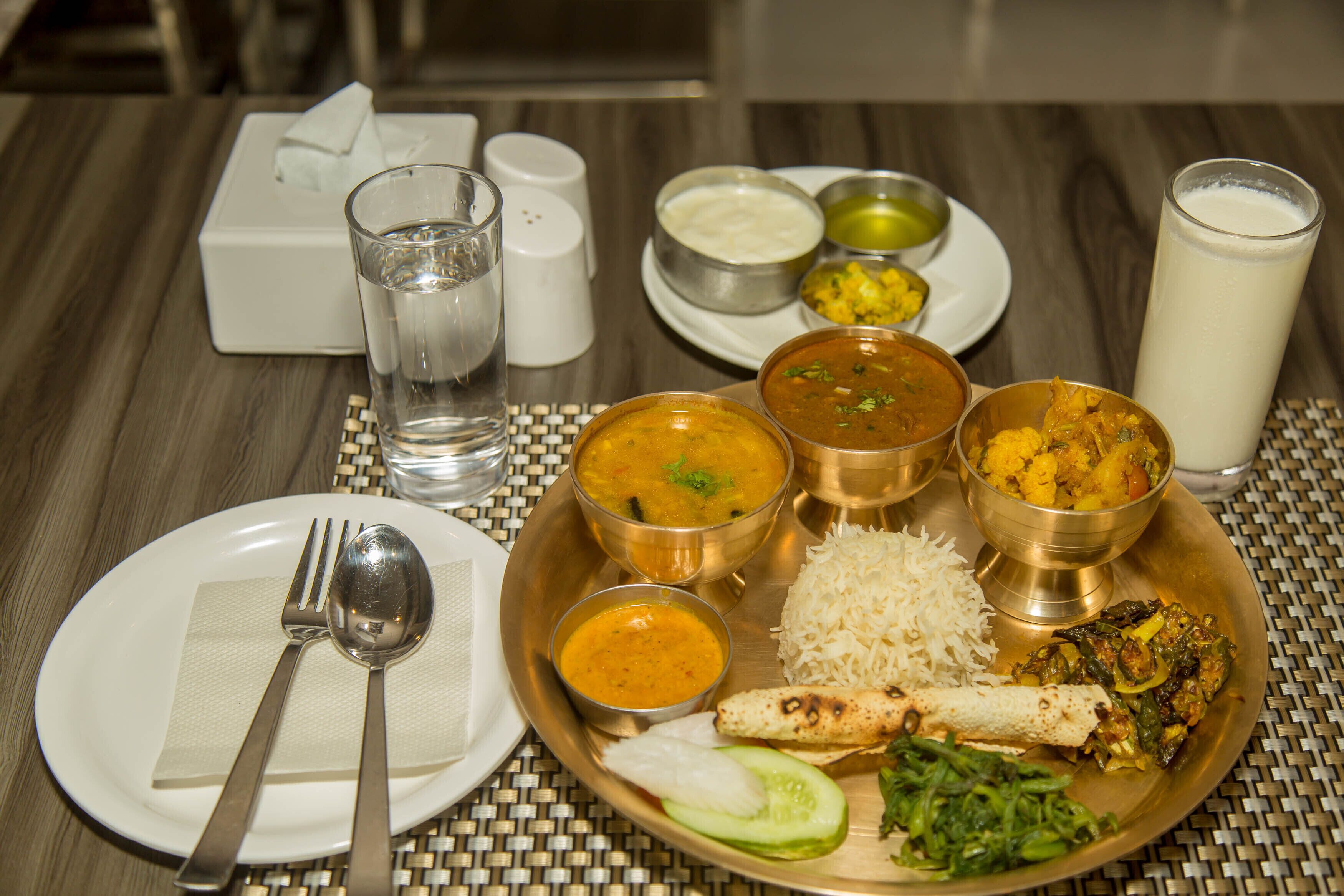 A table with a meal consisting of rice, various curries, and a glass of milk.