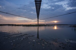 A large, modern structure with a unique geometric design, spanning across a body of water with a sunset in the background.