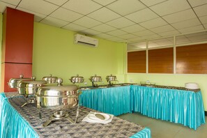 A buffet setup with multiple serving stations, a tiled ceiling, and a window with blinds.