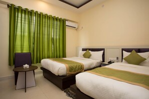 A hotel room with two beds, a small table, a chair, and an air conditioning unit on the wall.