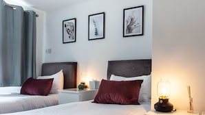 A hotel room with two beds, a nightstand with a lamp, and three framed pictures on the wall. - Great Havers (Bishop's Stortford)