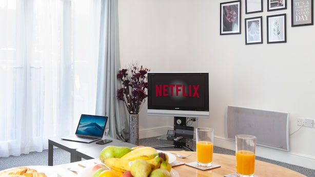 A breakfast setup with a laptop, a TV displaying 'NETFLIX', and a fruit bowl on a table. - Great Havers (Bishop's Stortford)