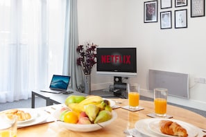 Een ontbijtje met een laptop, een televisie waarop 'NETFLIX' staat en een fruitschaal op een tafel.