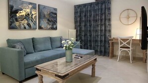 A living room with a sofa, a coffee table with a vase of flowers, a desk with a chair, and two wall-mounted paintings. - Best House Anakreontos (Nikaia-Agios Ioannis Rentis)