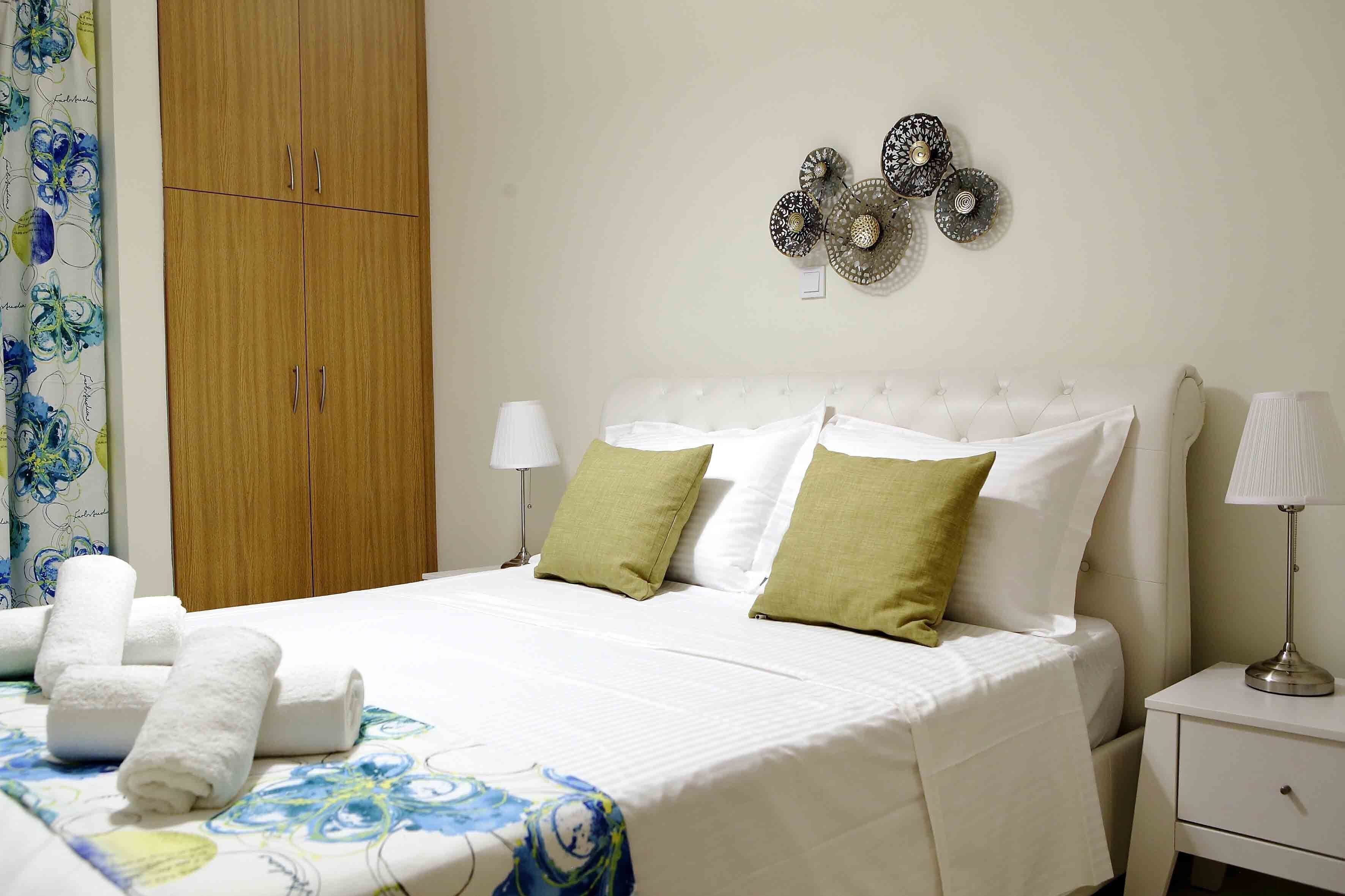 A neatly made bed with white bedding and green pillows, a wooden wardrobe, and decorative wall art.