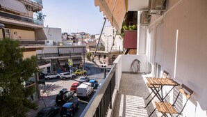 A balcony with a view of a busy street, a small table, and a chair. - Best House Anakreontos (Nikaia-Agios Ioannis Rentis)