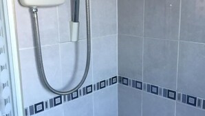 A bathroom with a shower, a handheld showerhead, and a bottle of shampoo on the floor. - Sturry House (Canterbury)