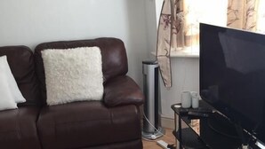A living room with a brown leather sofa, a white fluffy rug, a standing heater, and a TV on a black stand. - Sturry House (Canterbury)