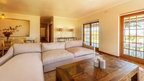 A living room with a large beige sectional sofa, a wooden coffee table, and a dining area with a small table and chairs. - Saxenburg Wine Farm (Cape Town)